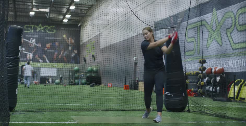A woman hits softballs indoors