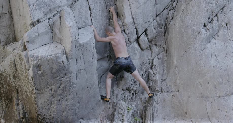 A man is climbing up a rock wall in a natural setting during the day