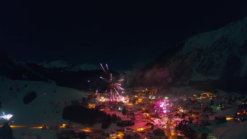 Fireworks are exploding in the sky over a village during a winter night