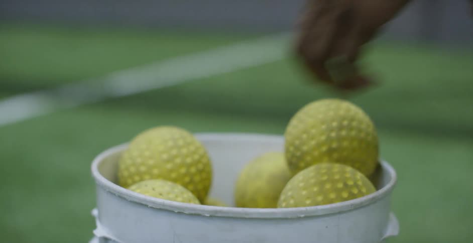 A person grabs softballs from a bin