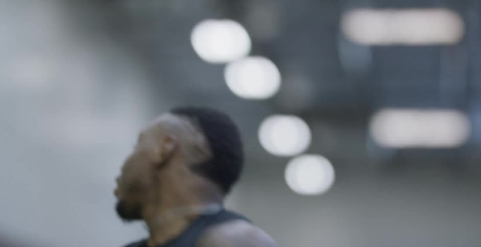 A male athlete is laughing and holding a football as he trains indoors