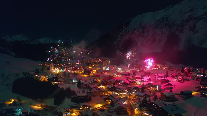 Fireworks are exploding in the sky over a village during a winter night
