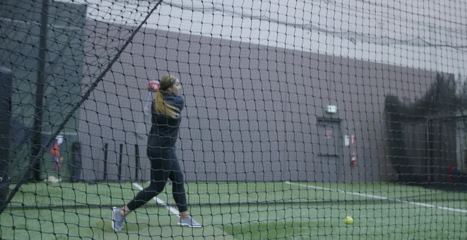 A woman is hitting some baseballs in a batting cage