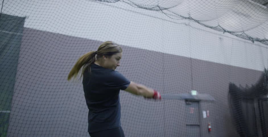 A female athlete is practicing batting in an indoor batting cage