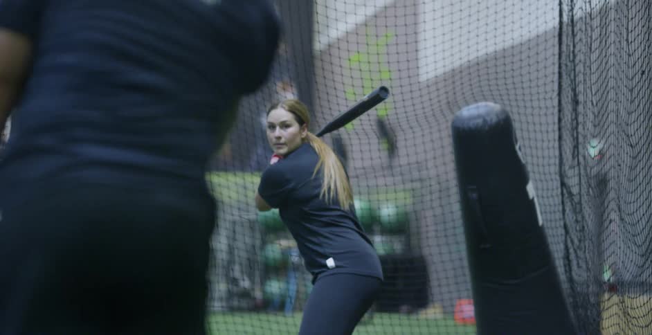 A woman hits a softball in a batting cage