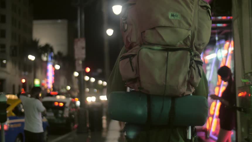 Man wearing large backpack walks down a city street at night