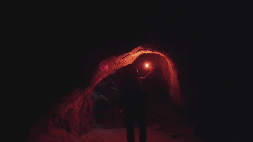 Man entering a dark cave with a lit flare
