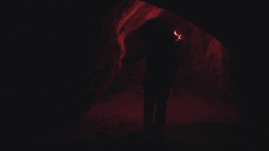 A person walks through a cave holding a flare