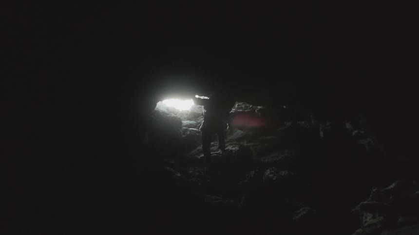 Man climbing some rocks towards the exit of a dark cave