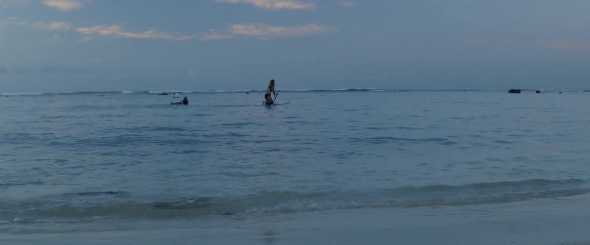 People on surfboards coming towards the shore on a cloudy day