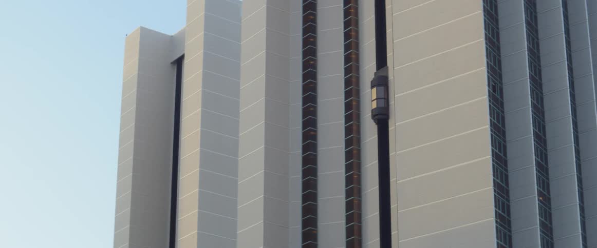 An elevator is going up and stopping on the side of a high rise building
