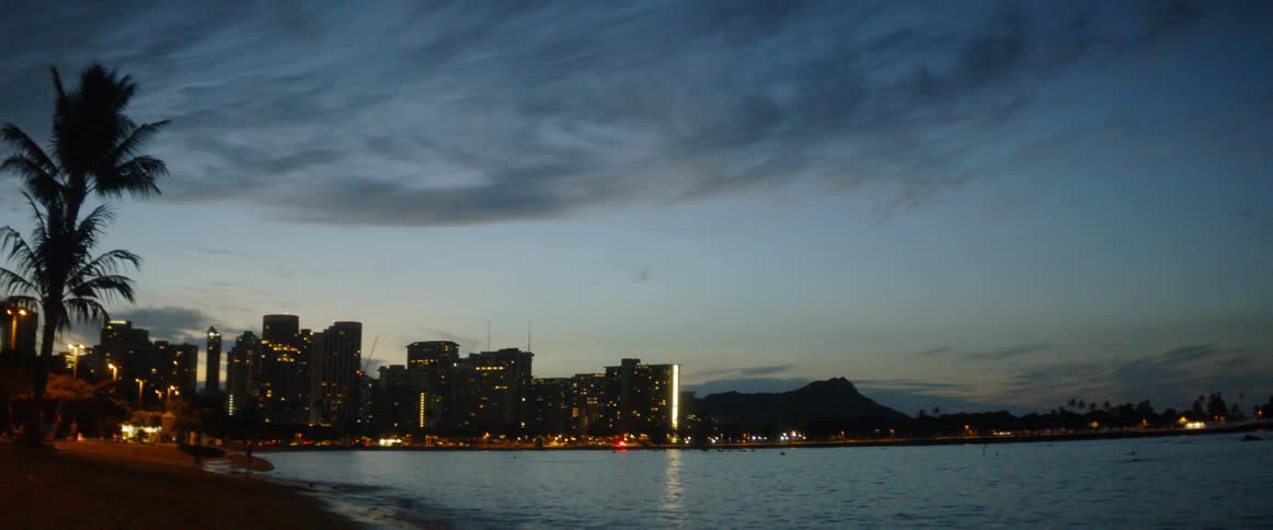 People carry their paddle boards into the ocean at a city beach at night