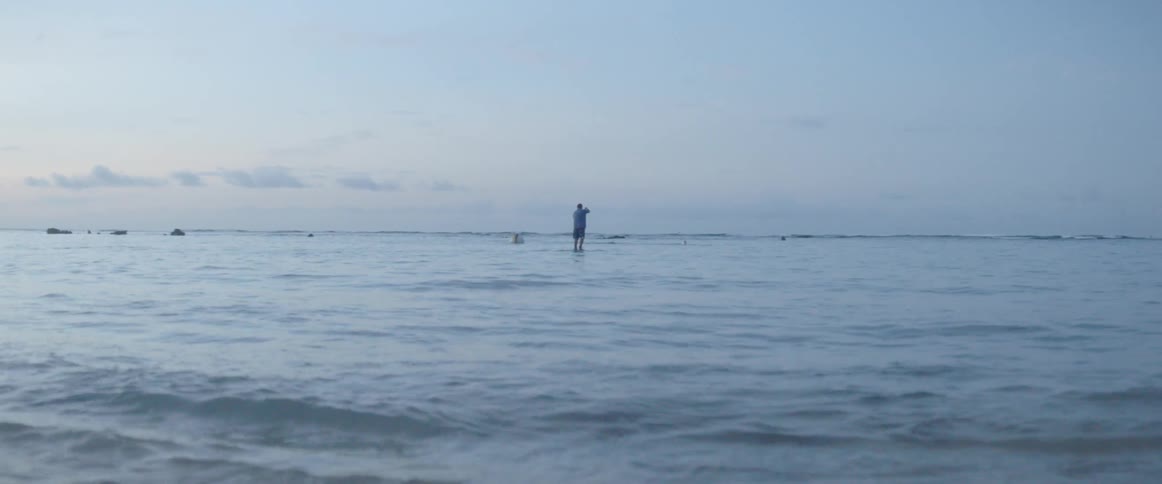 A man stands on a paddle board and rows