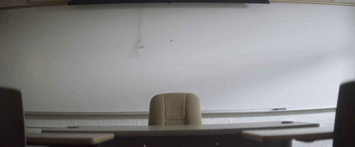 The cord from a screen sways against the board in an empty classroom