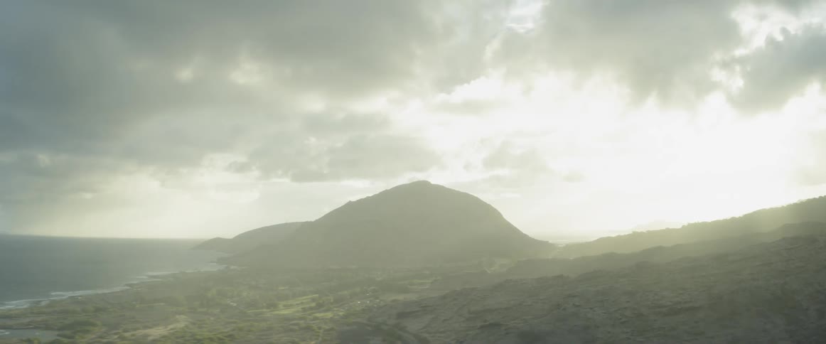 Sunlight shines through the clouds onto hills near the ocean