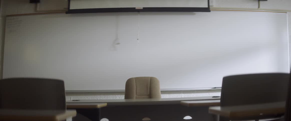 The projection screen cord sways against the board in an empty classroom