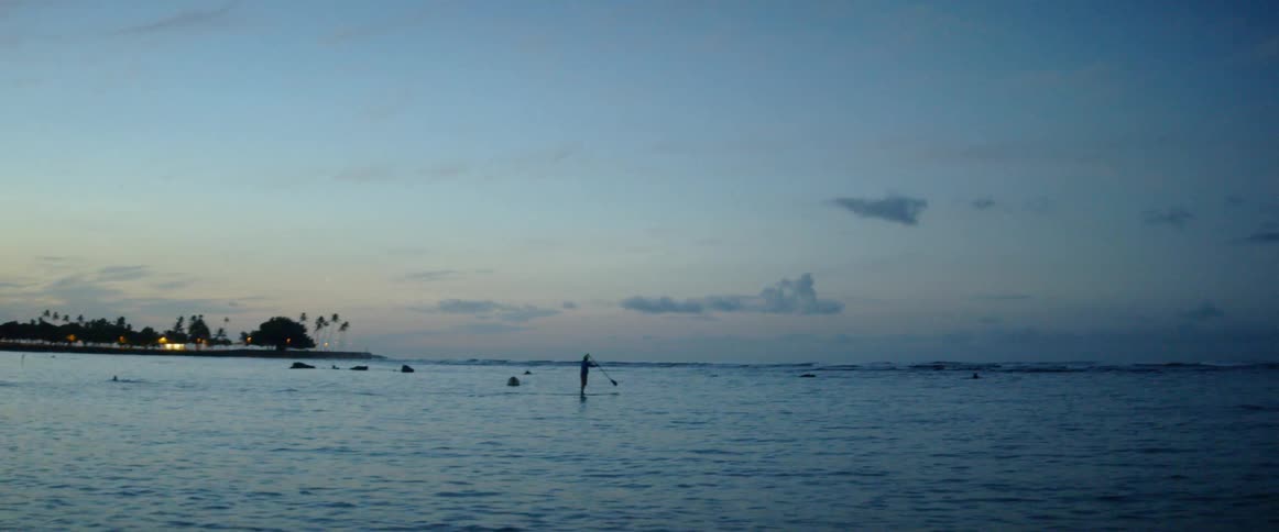 A person floats on a paddle board at sunset