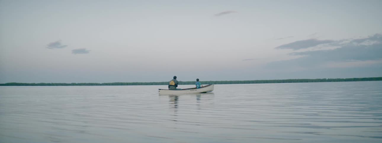 A man and child ride in a canoe at sunset
