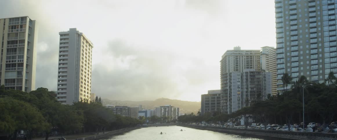Rowing skulls are moving down a river in a city during the day