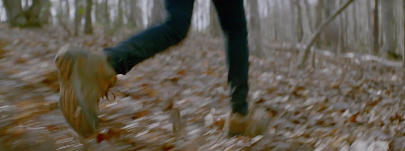People run through forest with fall leaves on the ground
