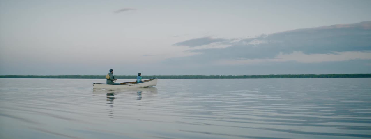Man and boy paddle canoe across a lake