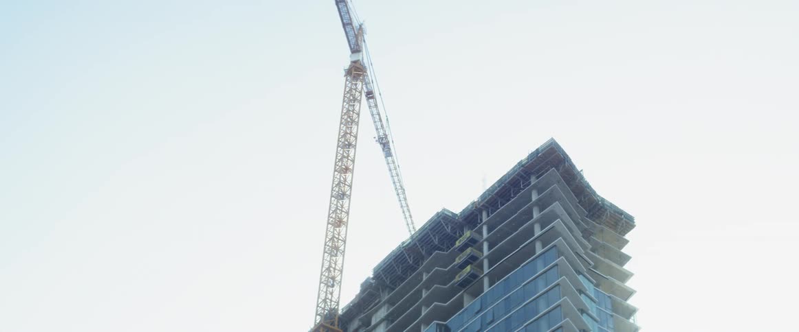 A construction crane is rotating its arm above the top floor of a building