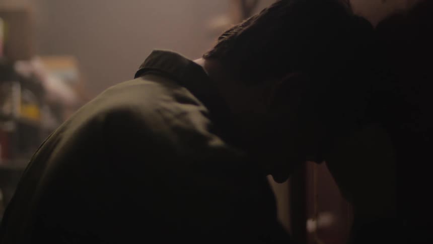 Man standing in a dark area leans head into wall