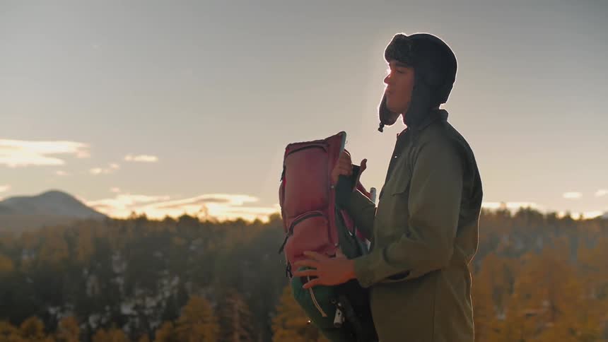 Man puts on his hat and backpack on a sunny day