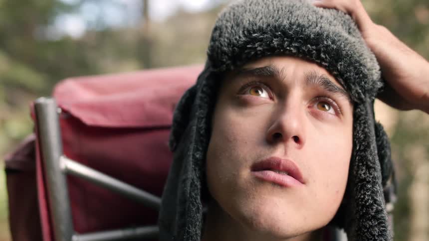 Man hiking looks up as he removes his hat