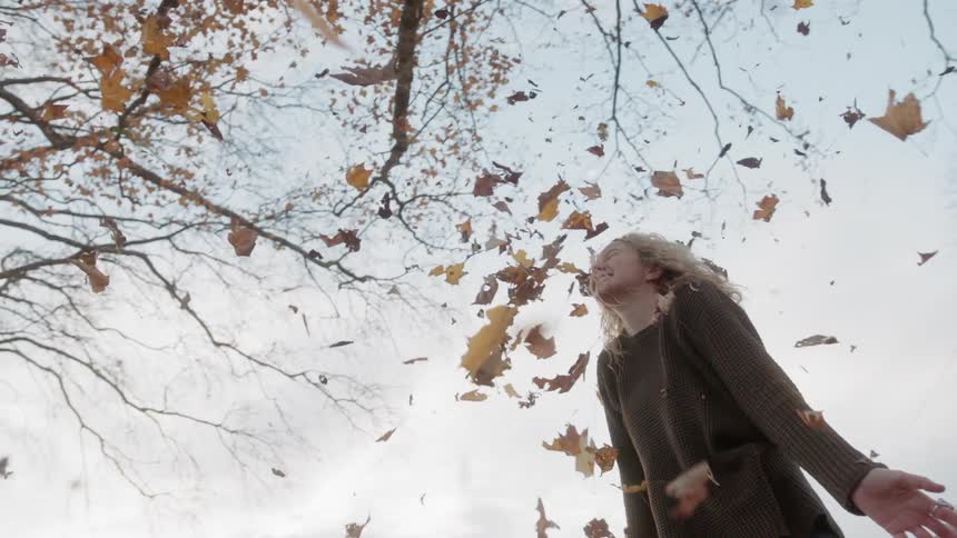 A man and woman throw autumn leaves into the air