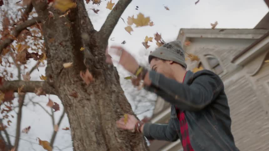 Man and woman throw leaves next to a tree outside in a yard