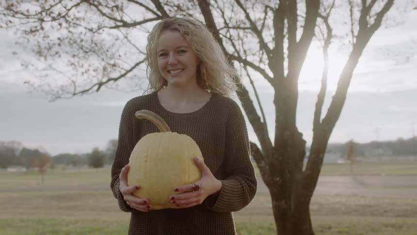 A woman holds a pumpkin outside under the sun