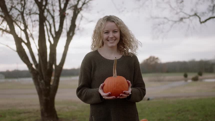 Woman smiles and holds a pumpkin
