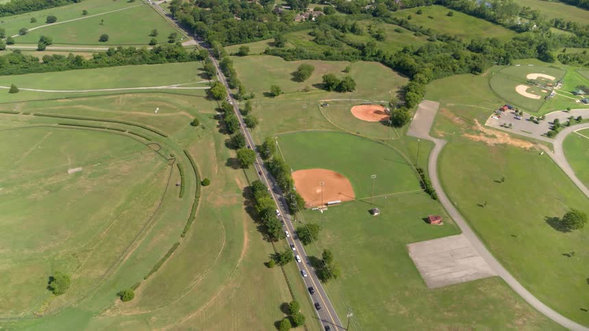 Cars drive down a highway that runs past a baseball field