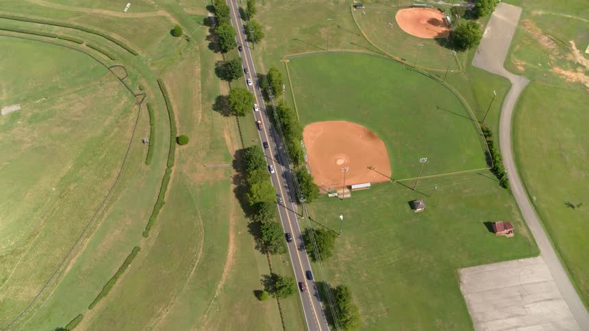 Vehicles commute on a road next to baseball fields