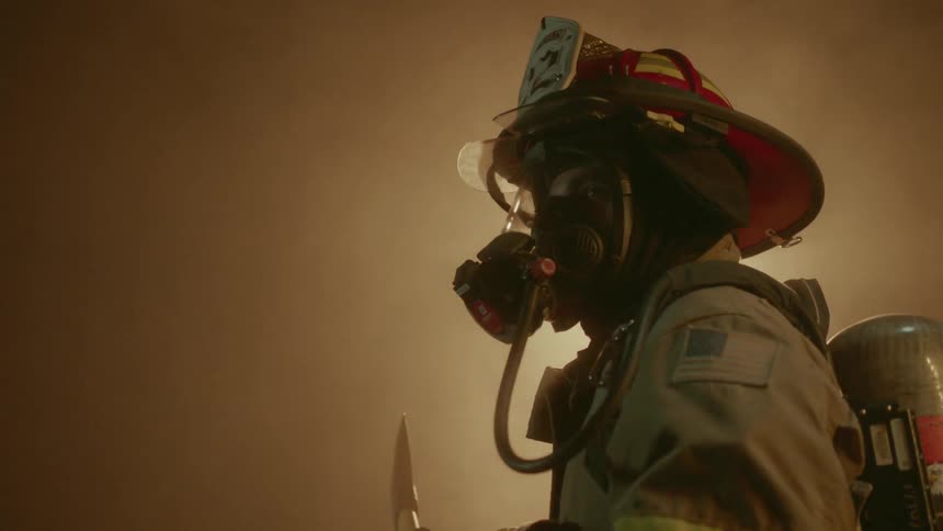 Firefighter holds ax and stands gazing at a fire