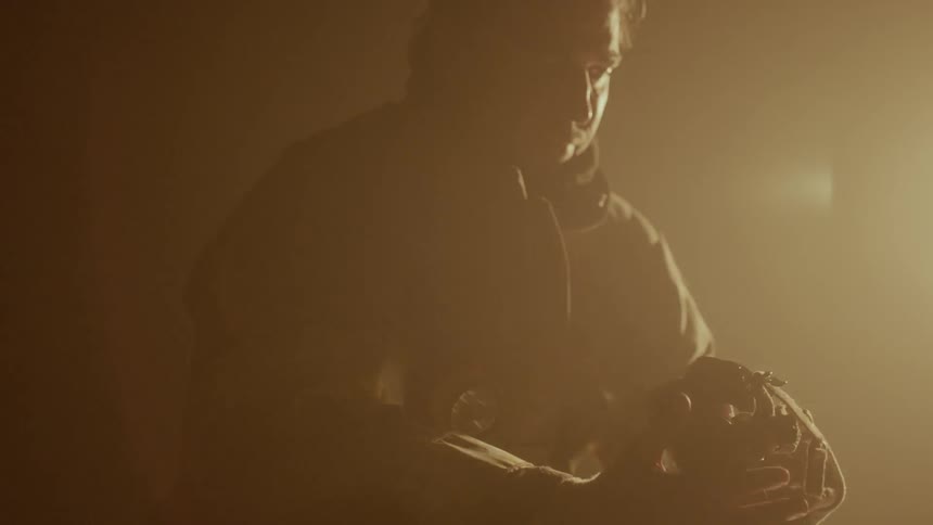 A firefighter is sitting in a darkened room looking at his mask
