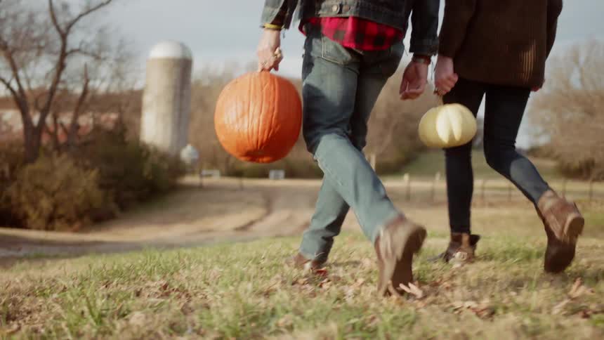 Man and woman walk towards a silo carrying pumpkins