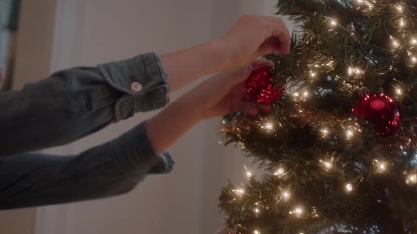 A boy and girl hang christmas ornaments on a tree
