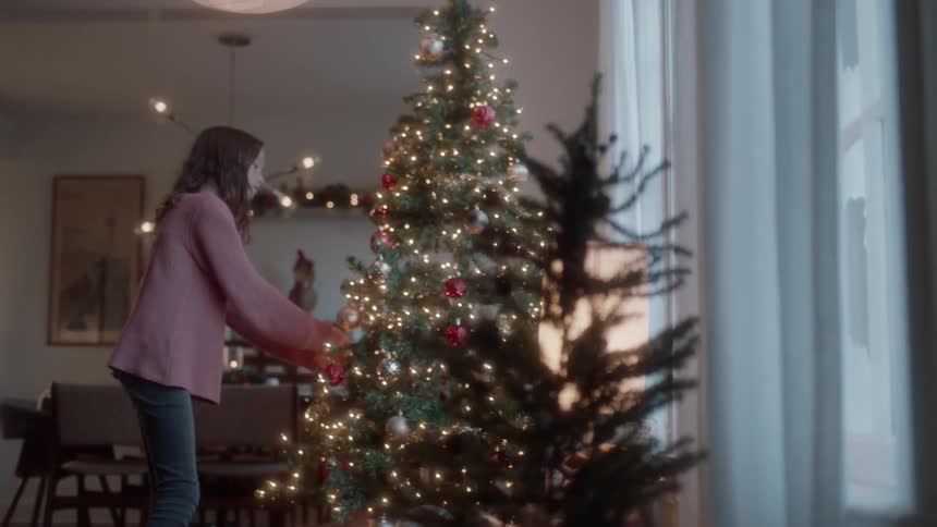 A girl hangs ornaments on a christmas tree