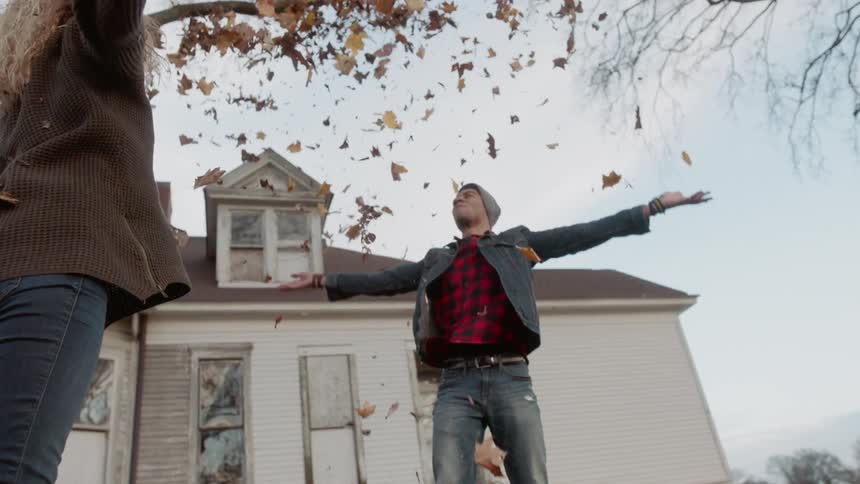 A man and woman playfully throw fallen leaves into the air