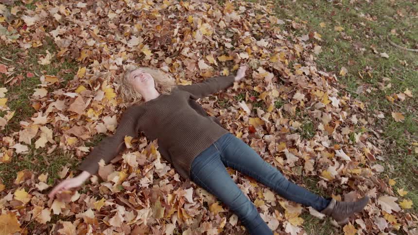 Woman lays in pile of leaves and makes an angel