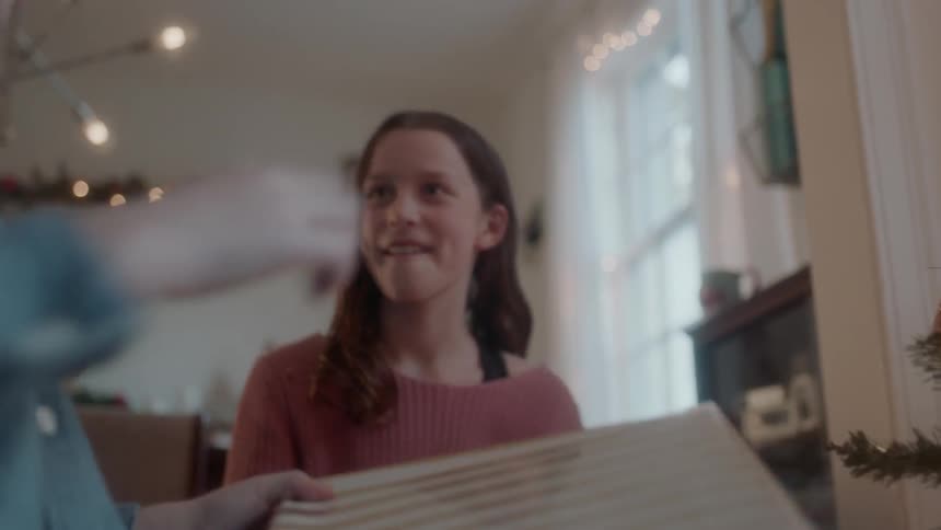 A boy shakes a wrapped gift then puts it back under the tree