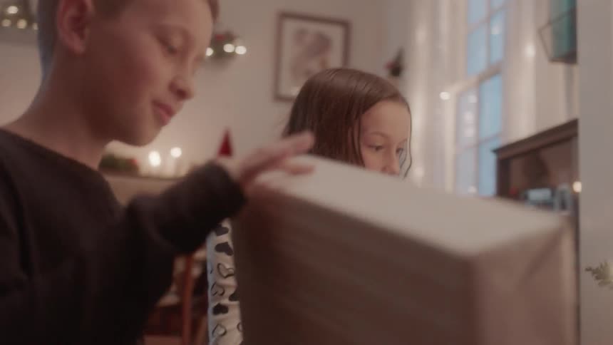 A boy and girl look at presents next to a christmas tree