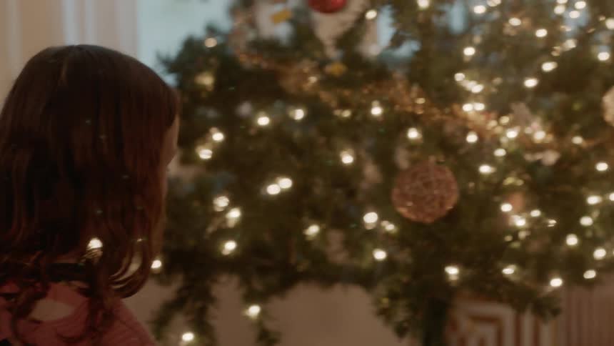 A girl and boy look at presents next to a christmas tree