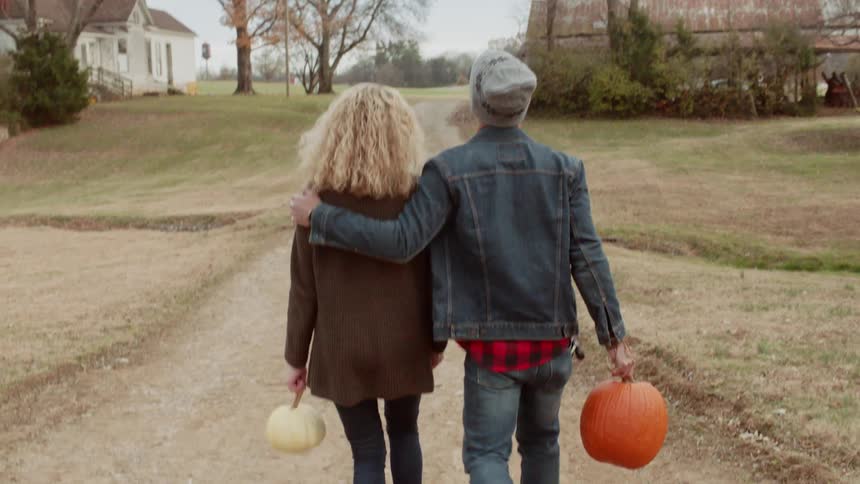 Man and woman walk on dirt path with pumpkins