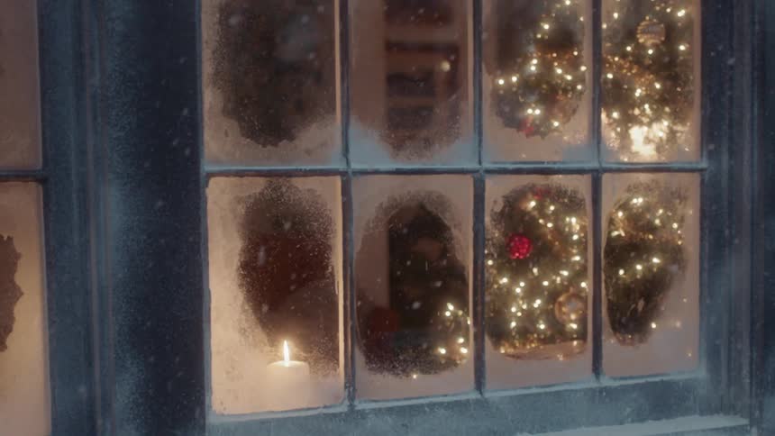 A lit christmas tree is visible through the snow frosted window panes