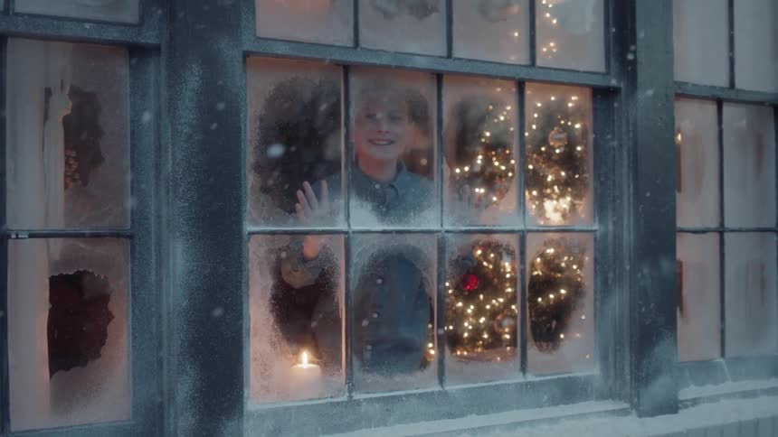 Boy looks outside a window to see it is snowing at christmas time