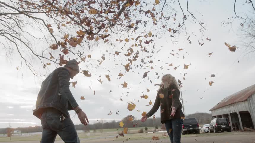 Man and woman play with a pile of fall leaves
