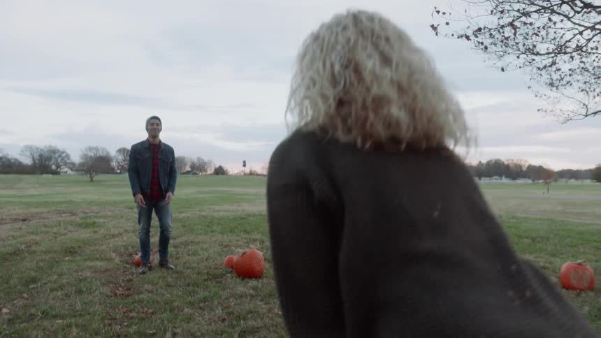 A man and woman throw a pumpkin back and forth
